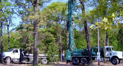An image of two trucks with large equipment drilling a well.
